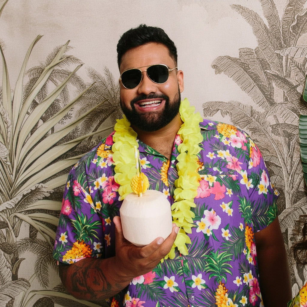 Person wearing a colorful shirt and yellow hawaiian flower lei tropical party accessory, holding a pineapple-shaped cup, with a tropical-themed background.
