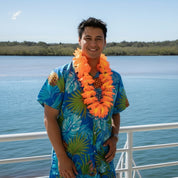 Person wearing a colorful shirt and orange hawaiian flower lei tropical party accessory,with water and blue sky in the background