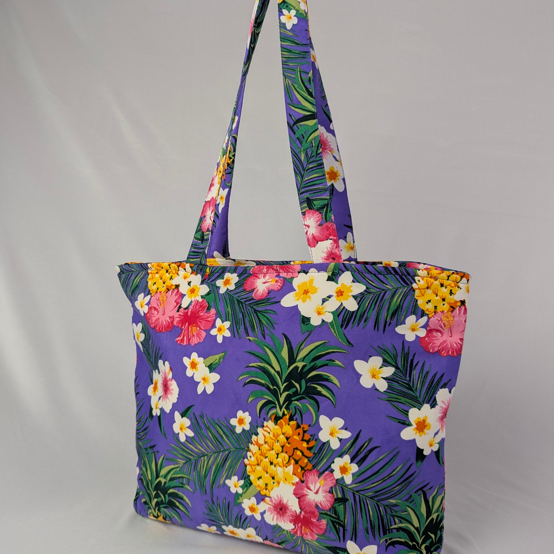 Purple Tropicool tote bag with floral and pineapple patterns on a light gray background, tropical style. | Tropicool Clothing