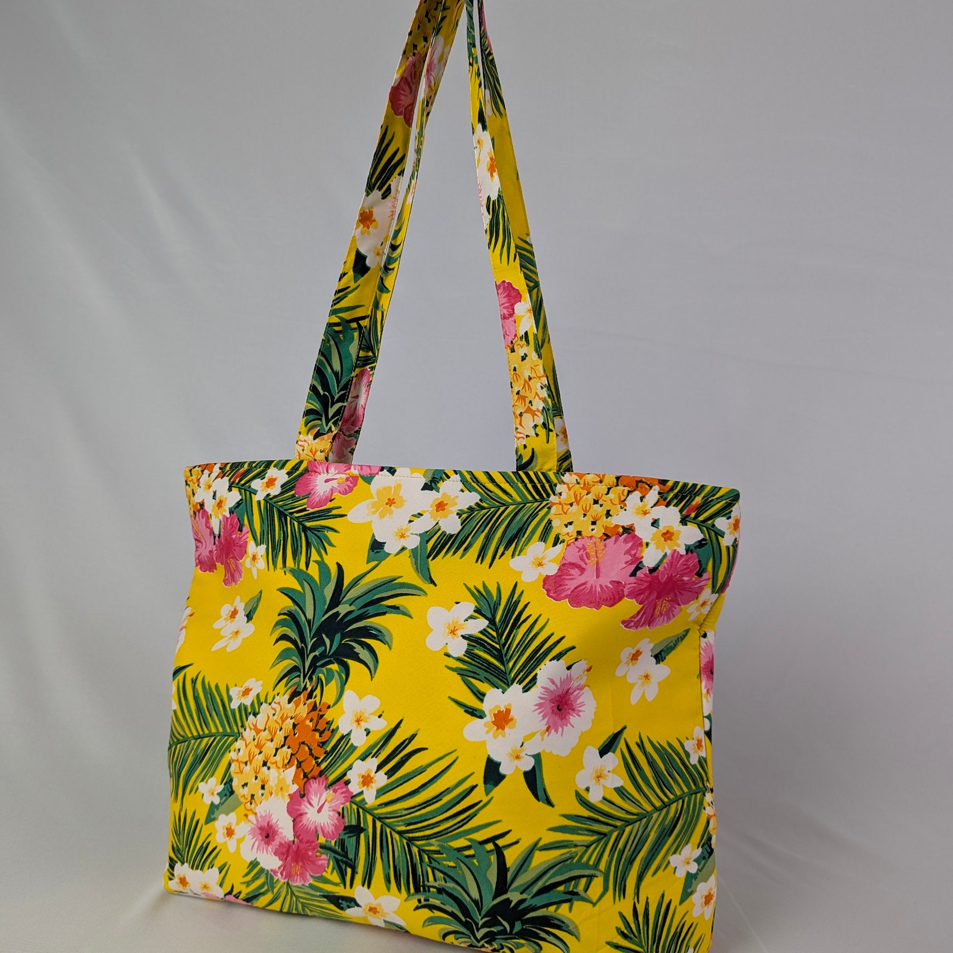 Tropicool Tote Bag with pink, white, and orange tropical flowers and green leaves on a light background. | Tropicool Clothing