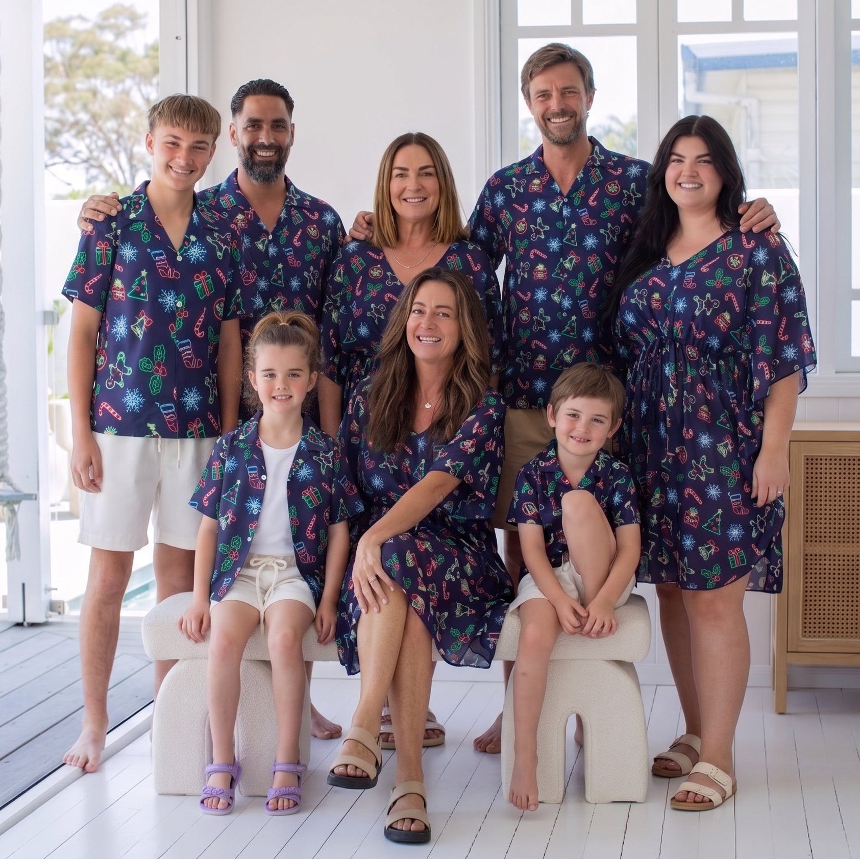 A family of seven posing together in matching dark blue tropical print swim shirts and swim shorts on a white-decked patio in front of a bright house.