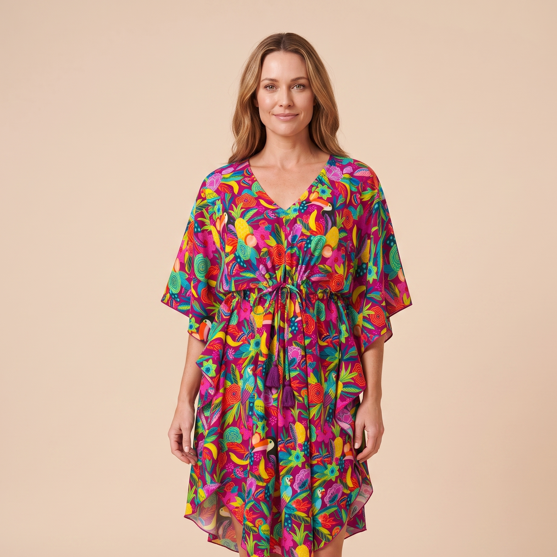 A woman modeling a short, V-neck dress with a colorful abstract floral print in shades of pink, purple, green, yellow, and blue, set against a solid beige studio background.