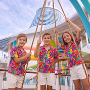 Three children standing on a cruise ship deck swing, wearing matching colorful tropical floral short-sleeve shirts and white shorts.