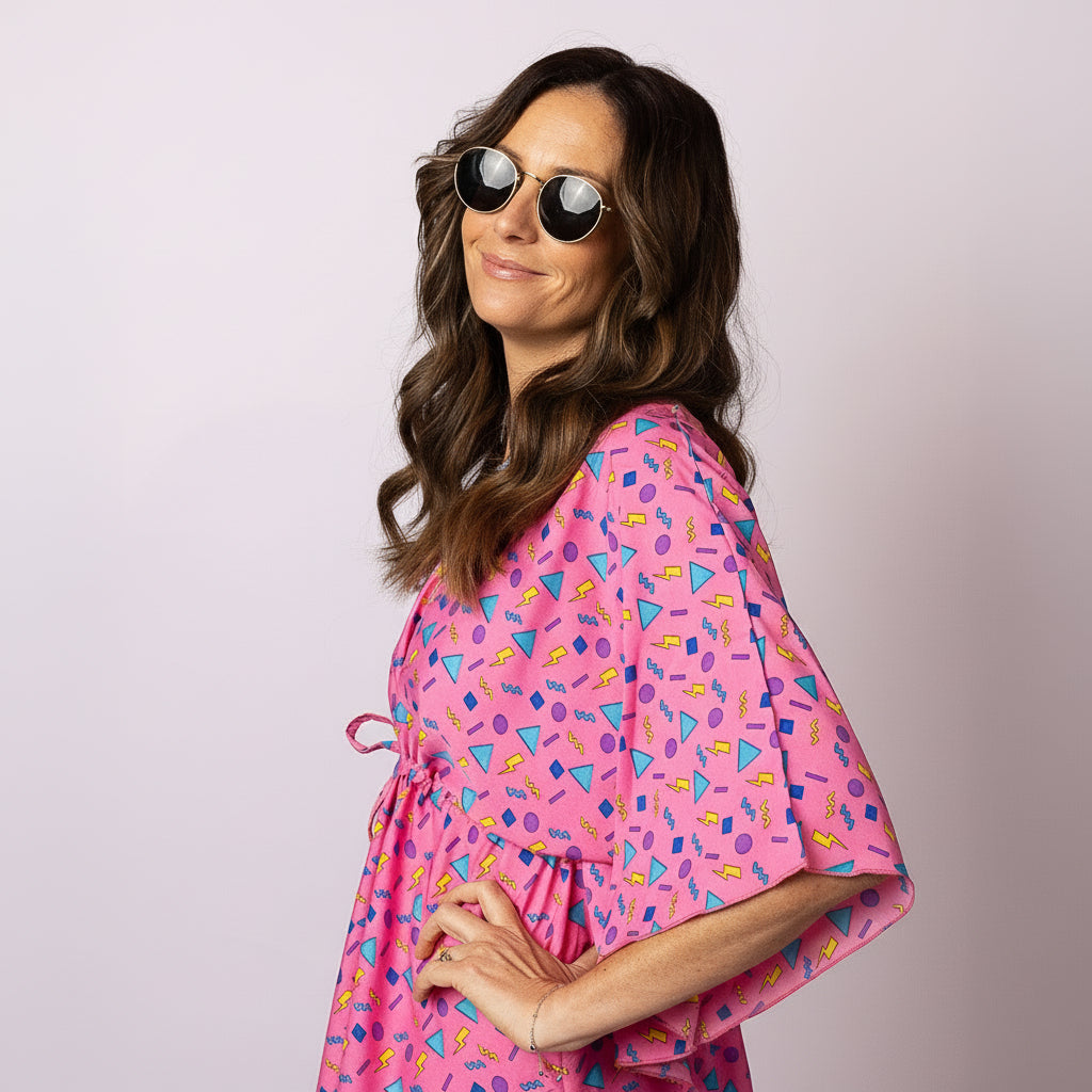 Woman in the pink Retro Vibe Kaftan by Tropicool, posing side-on with round sunglasses, highlighting the vibrant retro pattern and breezy kaftan style.